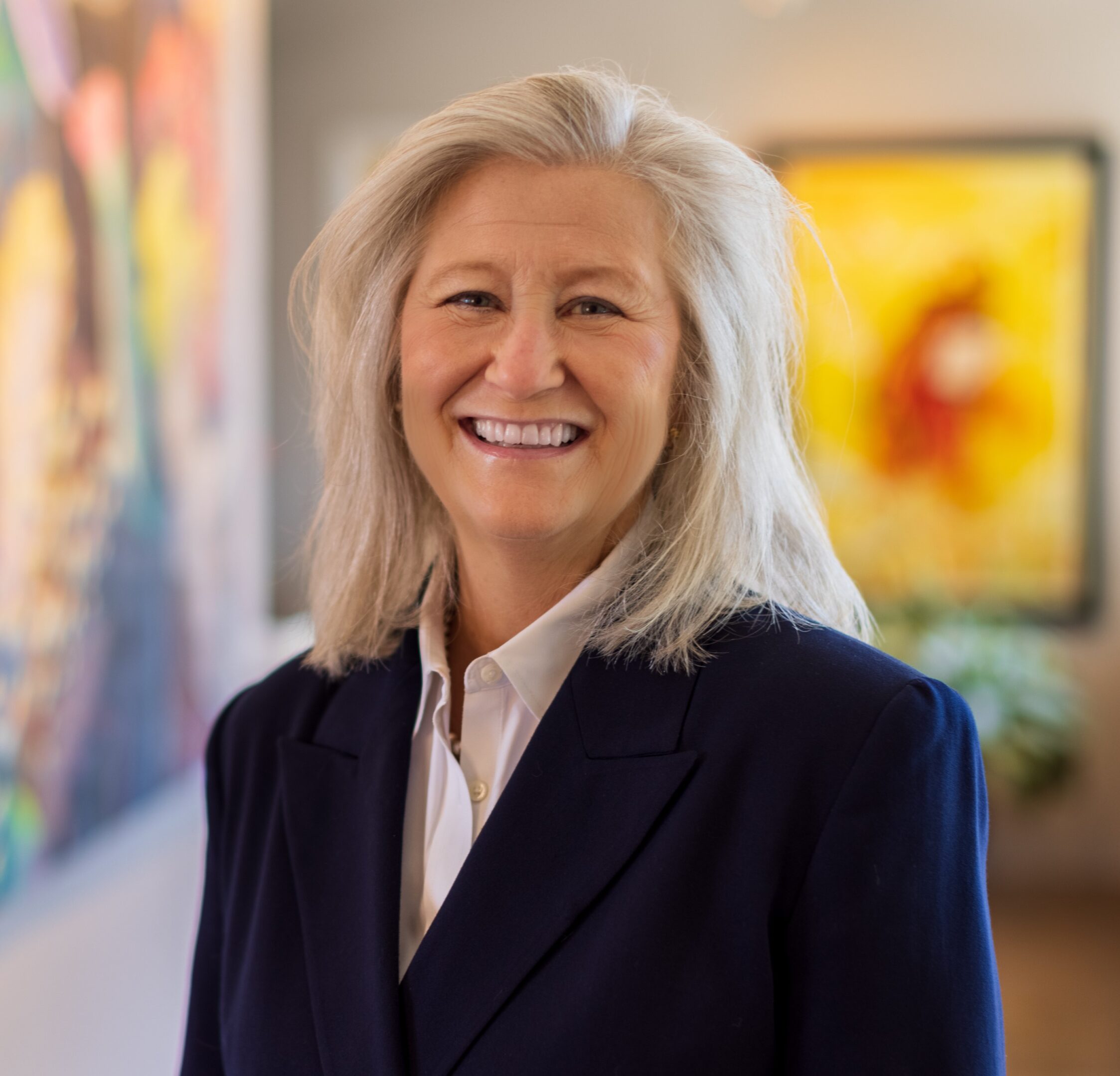 Smiling professional woman with gray hair in a dark blazer.