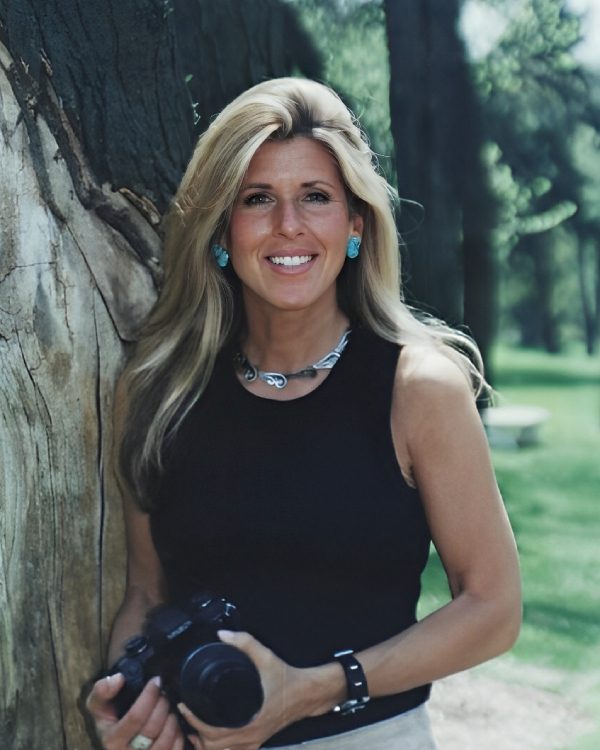 Smiling woman with camera near tree outdoors.