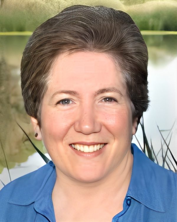 Smiling person outdoors with short hair.