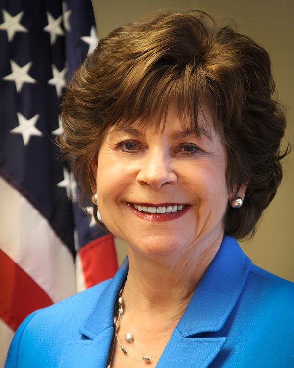 Smiling woman in blue blazer, flag background.
