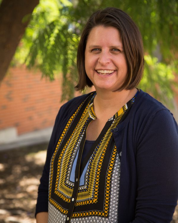 Smiling woman outdoors with leafy background.