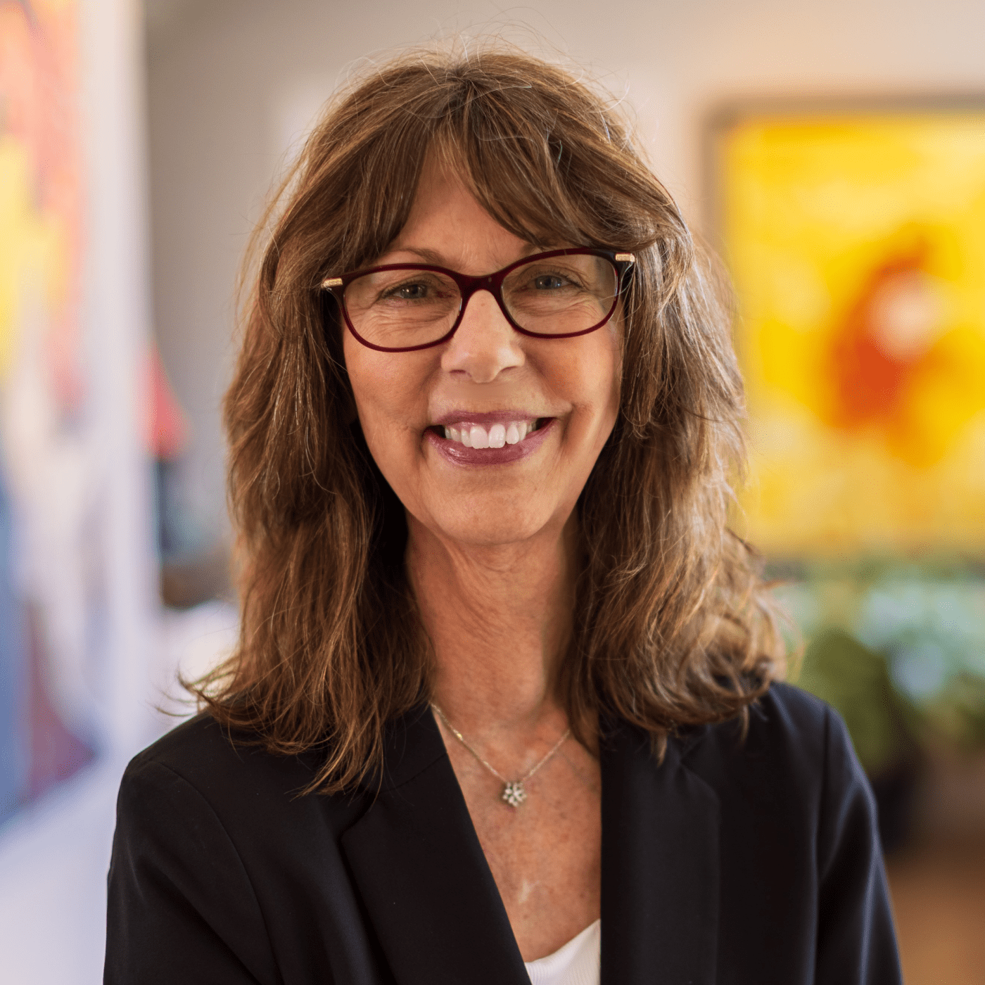 Smiling woman with glasses in a bright, colorful indoor space.