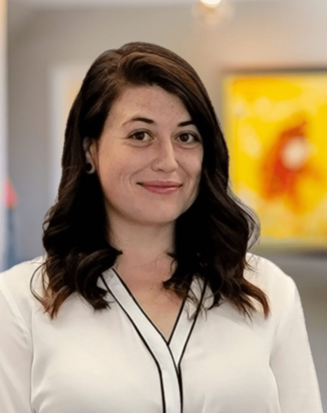 A woman with dark hair smiles gently in a bright indoor setting.